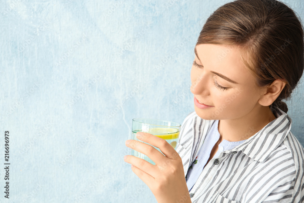 Young woman drinking water with lemon against color background Young woman drinking water with lemon against color background