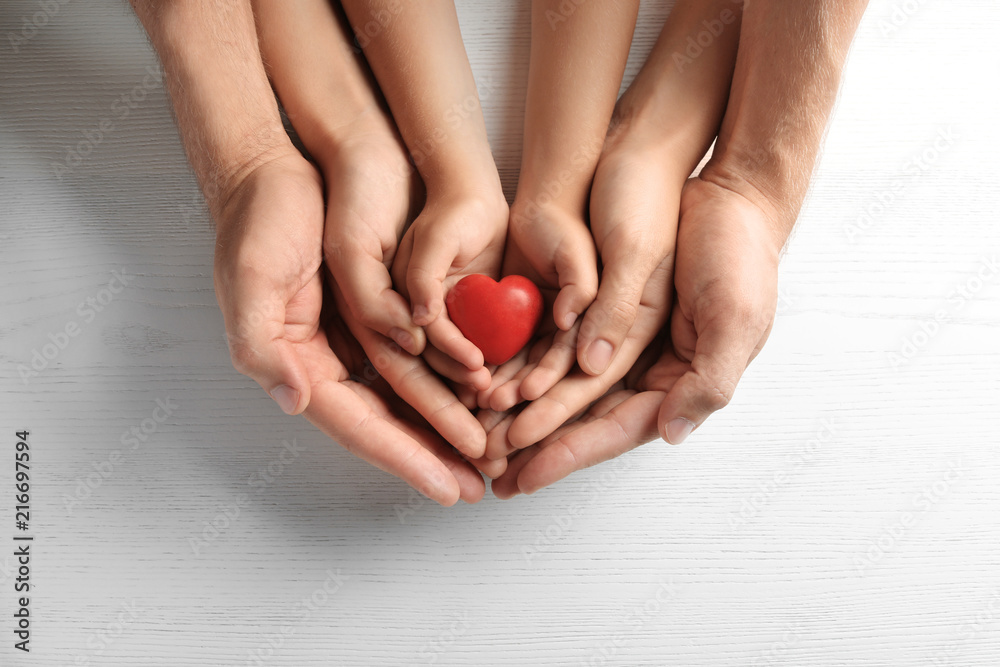 Family holding small red heart in hands on wooden background Family holding small red heart in hands on wooden background