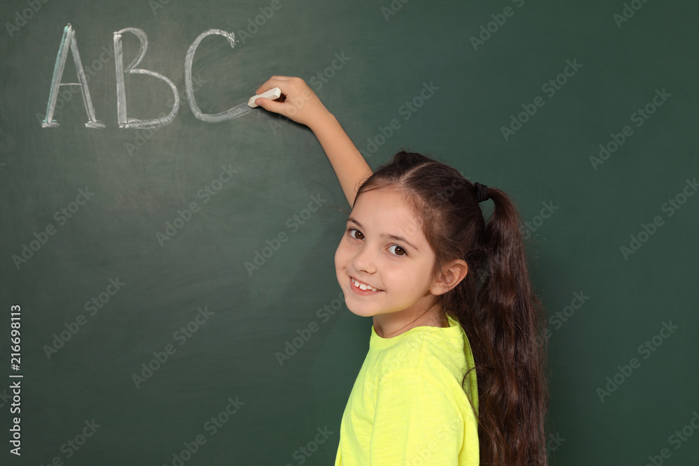 Little school child writing with chalk on blackboard