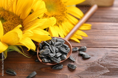 Spoon with sunflower seeds on wooden table, closeup