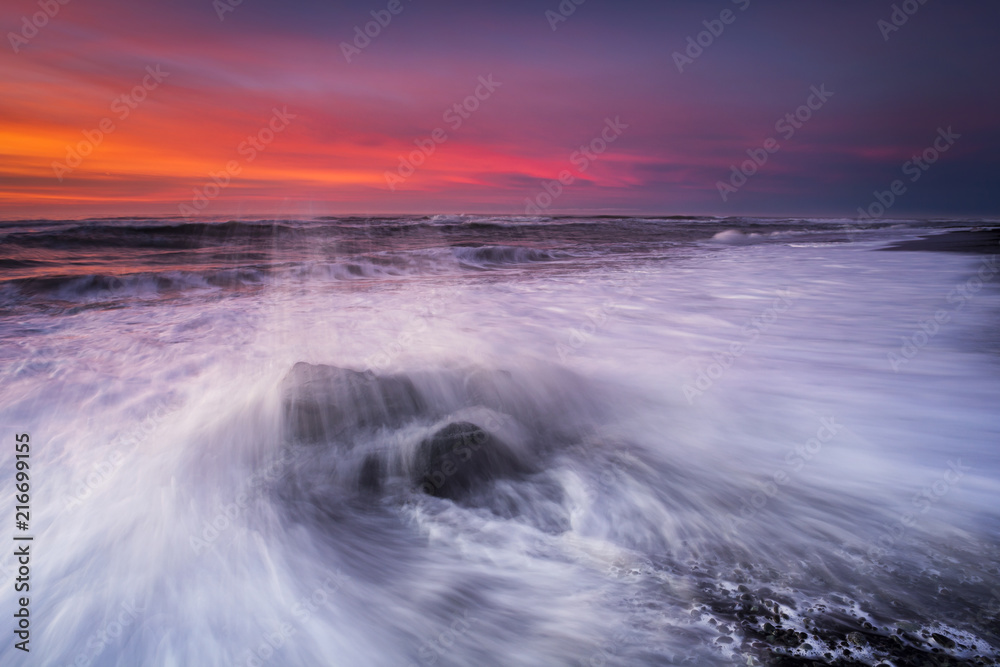 Jokulsarlon beach at sunrise, long exposure photography with waves and pieces of ice on the black sand beach.