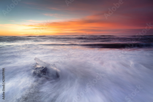 Jokulsarlon beach at sunrise, long exposure photography with waves and pieces of ice on the black sand beach.