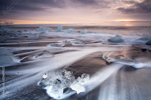 Jokulsarlon beach at sunrise, long exposure photography with waves and pieces of ice on the black sand beach. photo