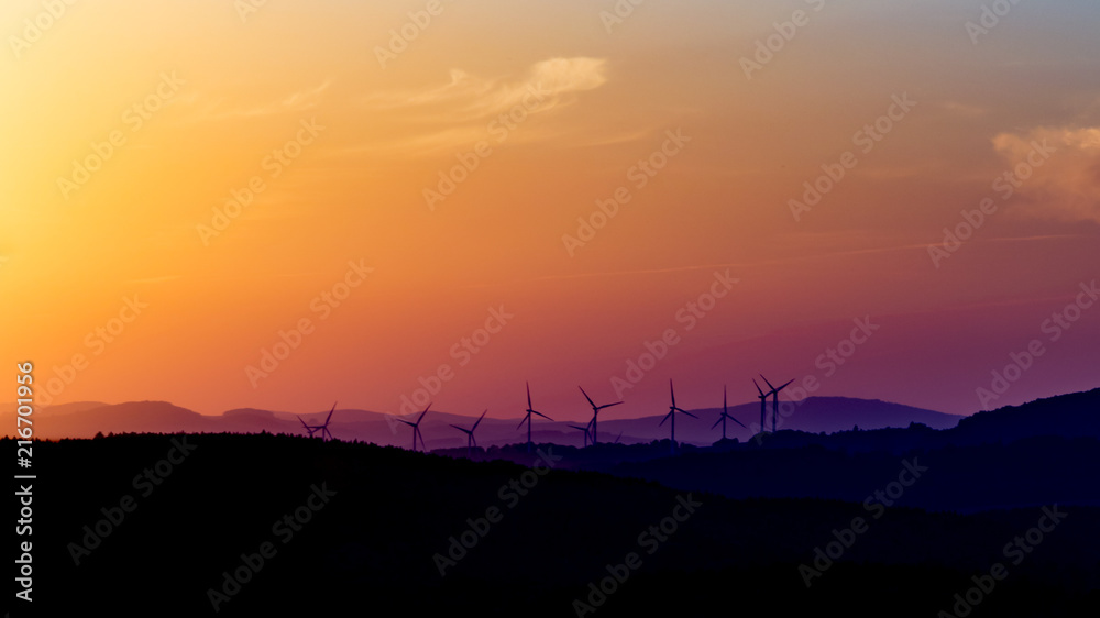 Sunset over the landscape with wind power plants. Sun tightly over the horizon.