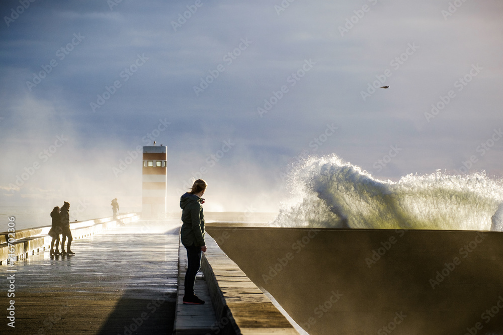 Super crazy waves over the pier in Porto, Portugal. Woman is watching big waves in the backlight. Bird flies over.