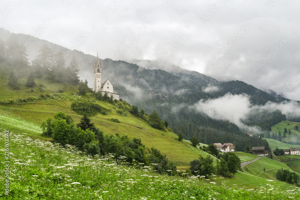Church on a misty hillside with a cloudy valley in the background in the Dolomites mountains in La Valle, South Tyrol, Italy	