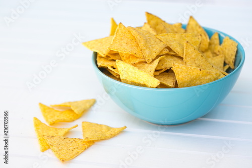 Yellow triangle shaped crispy nachos in a blue turquoise bowl placed on white table, copy space, some nachos laying out