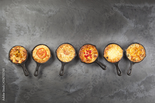 Six quiches in cast iron pans on a dark slate effect surface