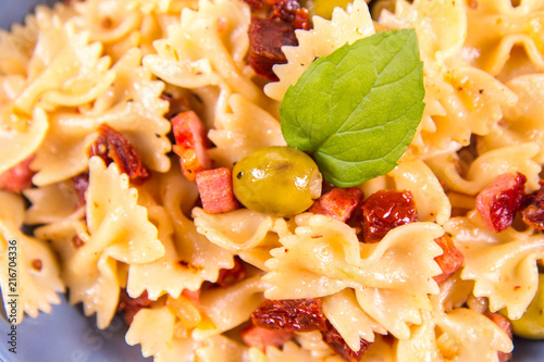 Farfalle pasta with sun dried tomato, ham and olives decorated with fresh mint