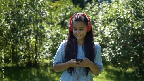 An attractive girl with long hair walks through the park and listens to music in headphones. Slow mothion. HD photo