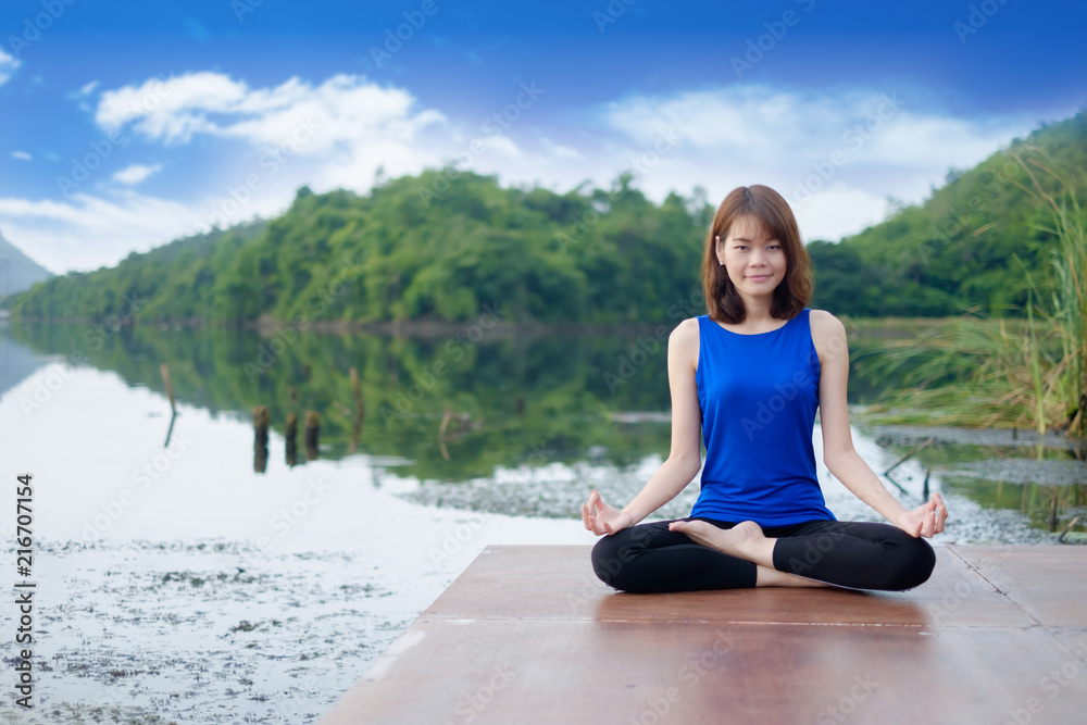 Young woman wear blue shirt exercising and sitting in yoga lotus position with nature background
