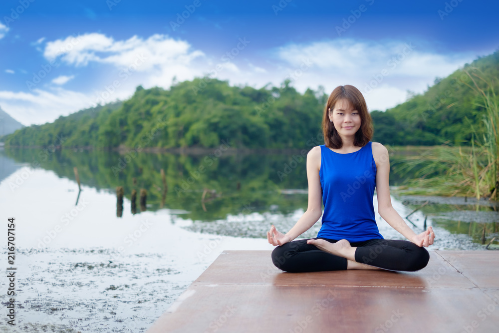Young woman wear blue shirt exercising and sitting in yoga lotus position with nature background Young woman wear blue shirt exercising and sitting in yoga lotus position with nature background