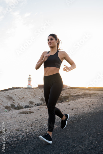 Woman running on a sand road past a lighthouse
