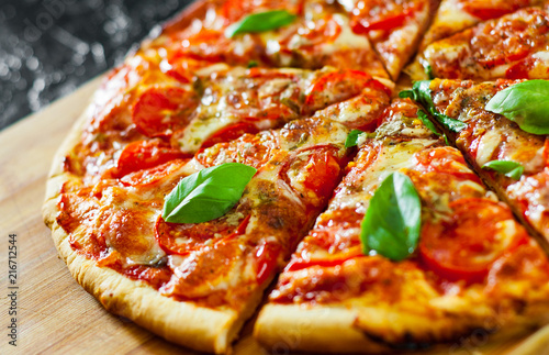 Fotografia sliced Pizza with Mozzarella cheese, Tomatoes, pepper, Spices and Fresh Basil