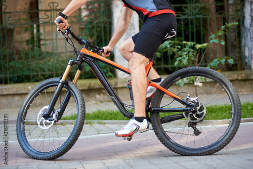 Crop view of male cyclist wearing professional sportswear riding bicycle along paved streets. Close up of sport bike on city streets. Concept of healthy lifestyle, outdoor training