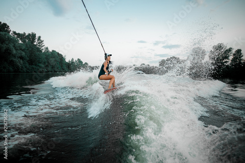 Young attractive girl riding on the wakesurf holding a rope of a motorboat © fesenko