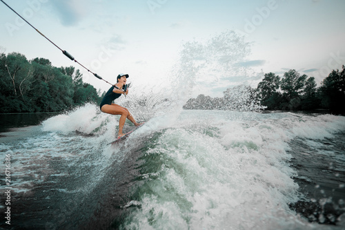 Young beautiful girl riding on the wakesurf holding a rope of a motorboat © fesenko