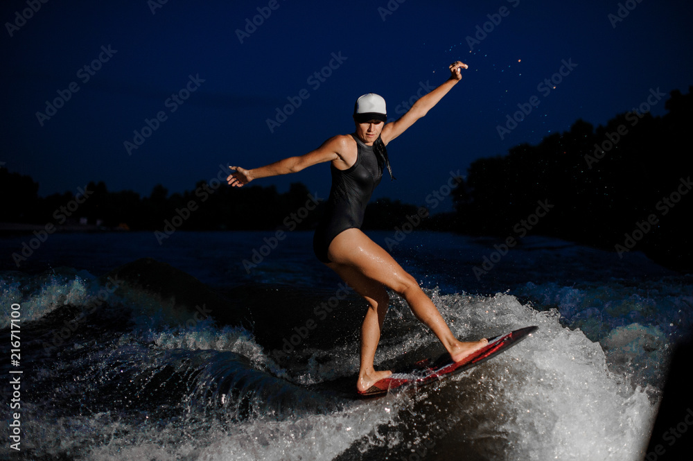 Rear view young active woman riding on the orange wakesurf in the night