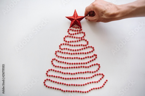 A person makes a creative Christmas or New Year tree made of beads in a minimalistic style and decorates with a star. Celebratory concept or creative idea or creativity.