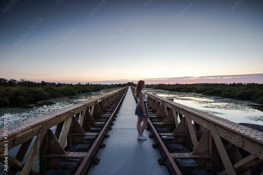 a women walking on a urban bridge looking at the sunset view at the lake