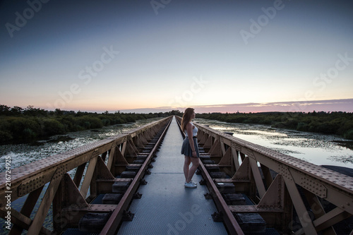 a women walking on a urban bridge looking at the sunset view at the lake