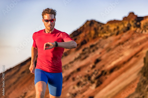 Fototapeta Naklejka Na Ścianę i Meble -  Athlete runner checking cardio on sports smartwatch jogging on outdoor run track. Running man wearing sunglasses and tech wearable device looking at watch during training workout.