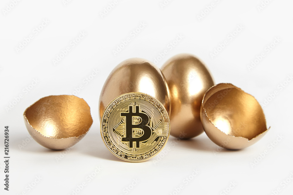 Bitcoin gold coin in golden egg shell. Broken egg on white background. Bitcoin virtual currency coin. Money, enrichment and profit concept Bitcoin gold coin in golden egg shell. Broken egg on white background. Bitcoin virtual currency coin. Money, enrichment and profit concept