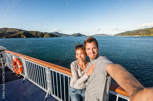 Cruise couple tourists taking selfie on New Zealand travel. People traveling on ferry boat Marlborough sounds taking self-portrait picture with mobile phone smiling at camera.