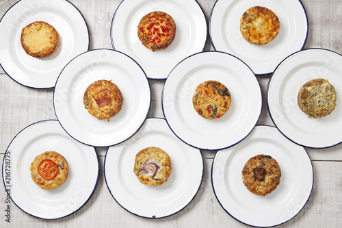 Individual quiches on white enamel plates on a light coloured tabletop