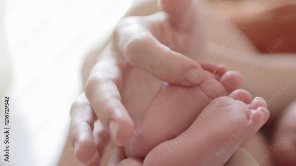 Young mother gently stroking the legs of her newborn baby Young mother gently stroking the legs of her newborn baby