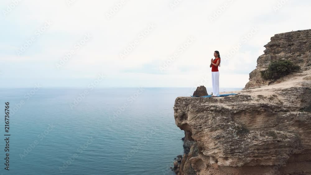 Woman standing and meditating on a cliff over the ocean. Yoga on the cliff.