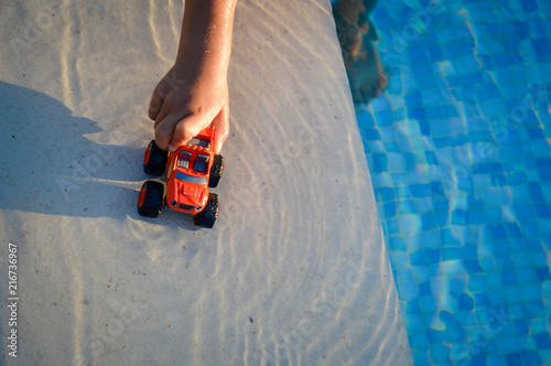 Defocused blurry closeup on child hand playing with car in the water splashing on sunny outdoors tropical background. Unfocused recreational happy kids having fun relax on travel vacation summertime.