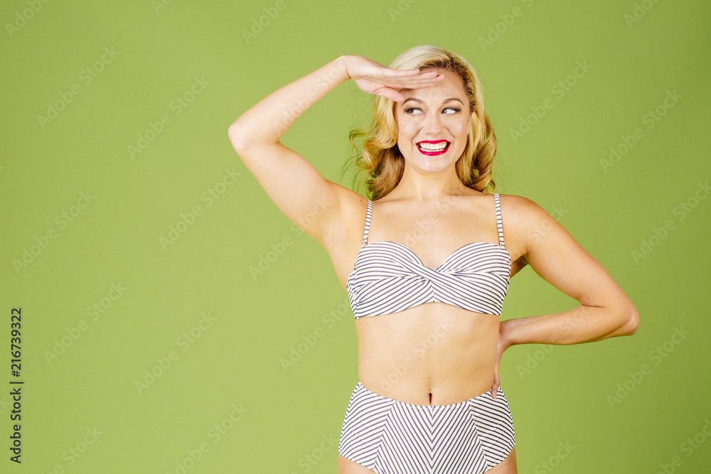 Blonde woman in bikini with hand by her forehead, isolated on green studio background Blonde woman in bikini with hand by her forehead, isolated on green studio background