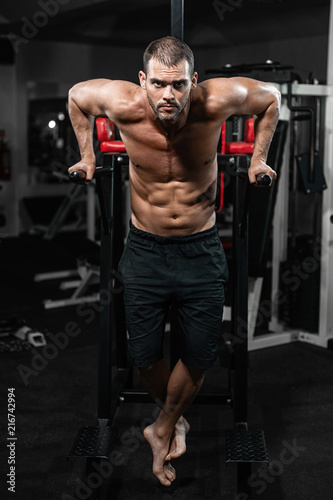 Muscular man doing push-ups on uneven bars in crossfit gym.