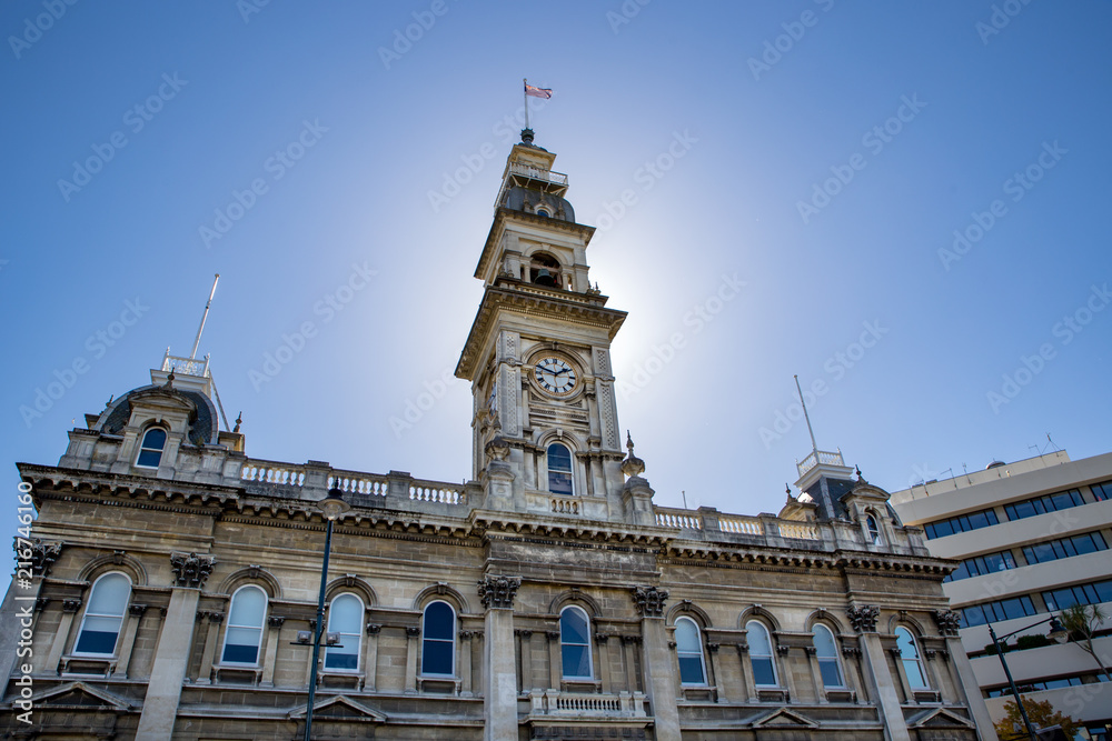 The clock tower on an old stone building in the city of Dunedin is lit up in the sunlight