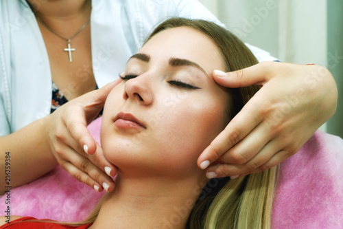 The girl doing the facial massage . Young beautiful woman on cosmetic procedures .