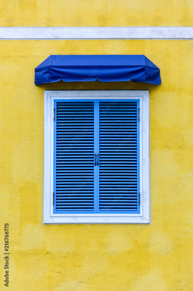 closed traditional blue greek window with white frame and blue fabric awning on yellow cement background, copy space