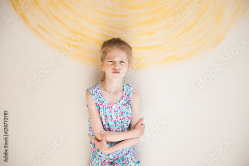 pretty upset little girl with grimace on her face vivid wall with painted sun