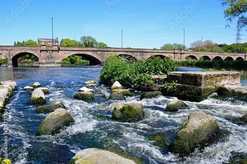 View across boulders and the weir towards the Trent Bridge road bridge A511 over the River Trent, Burton upon Trent, UK.