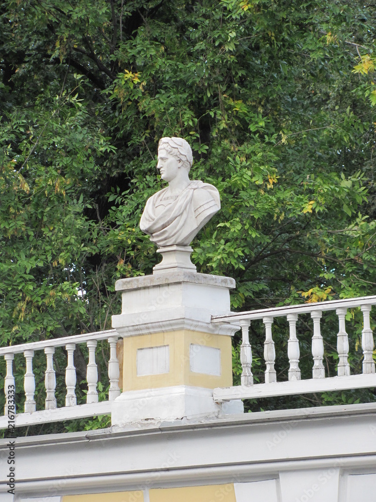 Obraz premium White statue on a park fence against a background of green trees