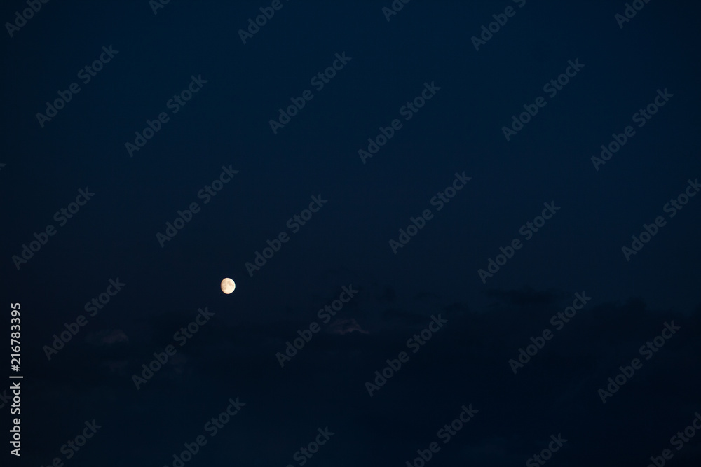 three-quarters of the growing moon on the navy blue sky background with some visible clouds in mystic mood three-quarters of the growing moon on the navy blue sky background with some visible clouds in mystic mood