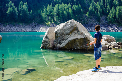 boy fishing in the high mountains in alpine lake, on a summer day, italy piedmont valley ossola