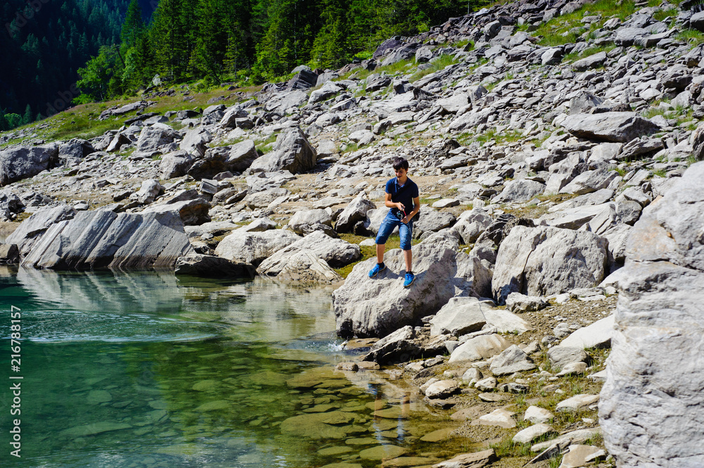 boy fishing in the high mountains in alpine lake, on a summer day, italy piedmont valley ossola