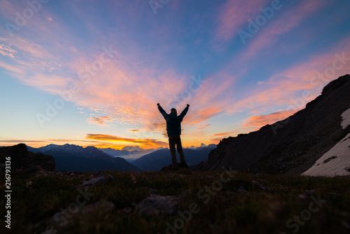 Man standing on mountain top outstretching arms, sunrise light colorful sky scenis landscape, conquering success leader concept. photo