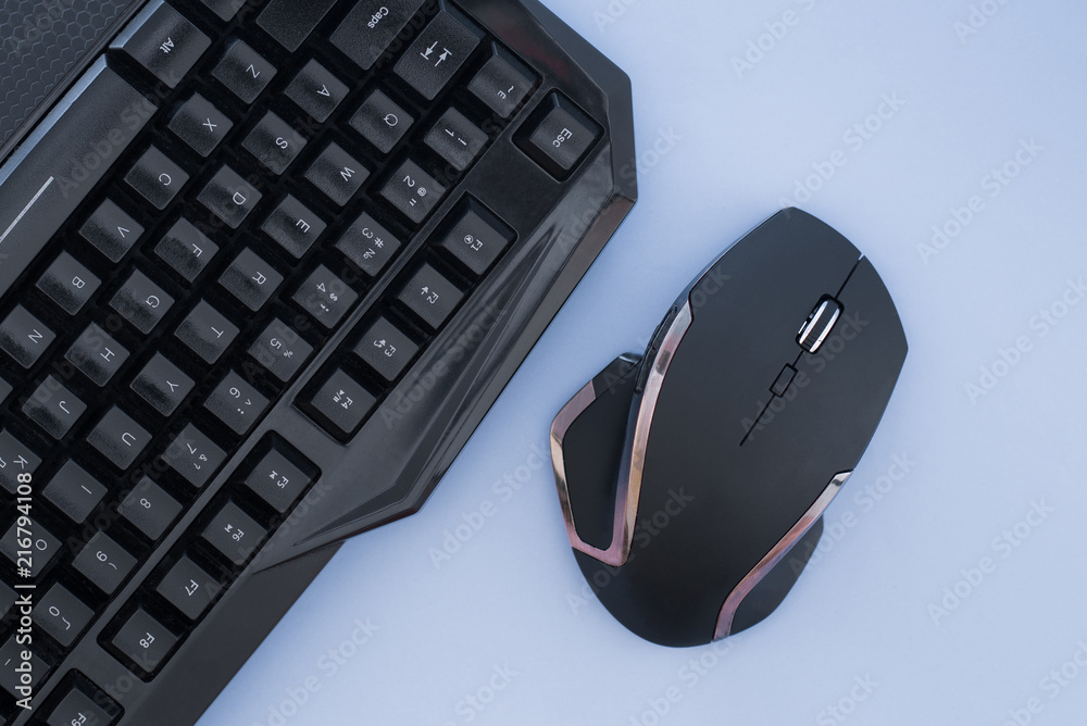 Black mouse and keyboard on a blue background, top view. Workplace, mouse and keyboard flat lay. Computer devices Black mouse and keyboard on a blue background, top view. Workplace, mouse and keyboard flat lay. Computer devices