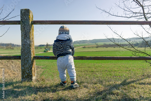 Toddler enjoying view into rural countryside in srping with tractor approching. photo