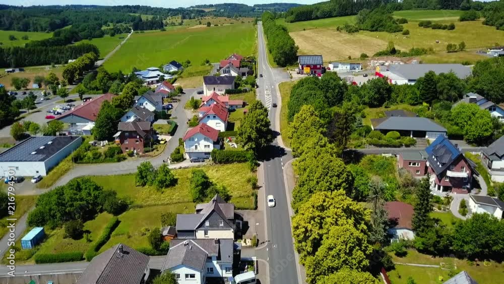 Aerial footage flying over houses and streets in rural community surrounded by green fields and rooftops.