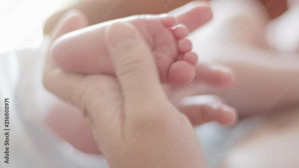 Young mother gently stroking the legs of her newborn baby Young mother gently stroking the legs of her newborn baby