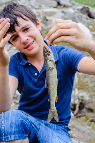 teen ager fisherman shows happy, catching an Salvelinus alpinus in an alpine lake
