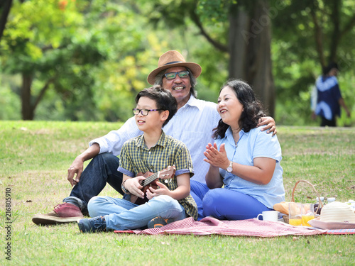 Grandparents spend the time in holiday with grandchildren at nature park.They are play guitar and singing together,Happy family concept.